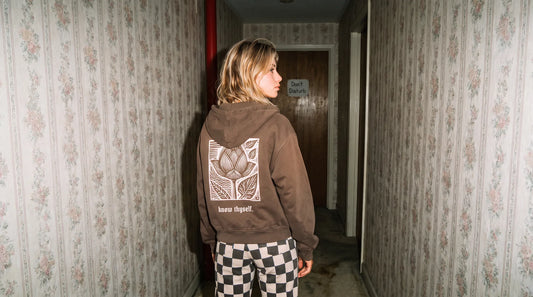 Woman in a vintage hallway showing the lotus woodcut back print of the "know thyself." zip hoodie