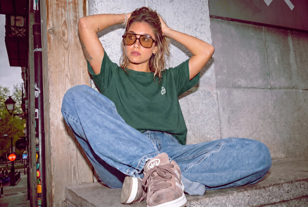 Woman in a green "Classical T*ts" waffle tee and baggy jeans sitting on a city ledge