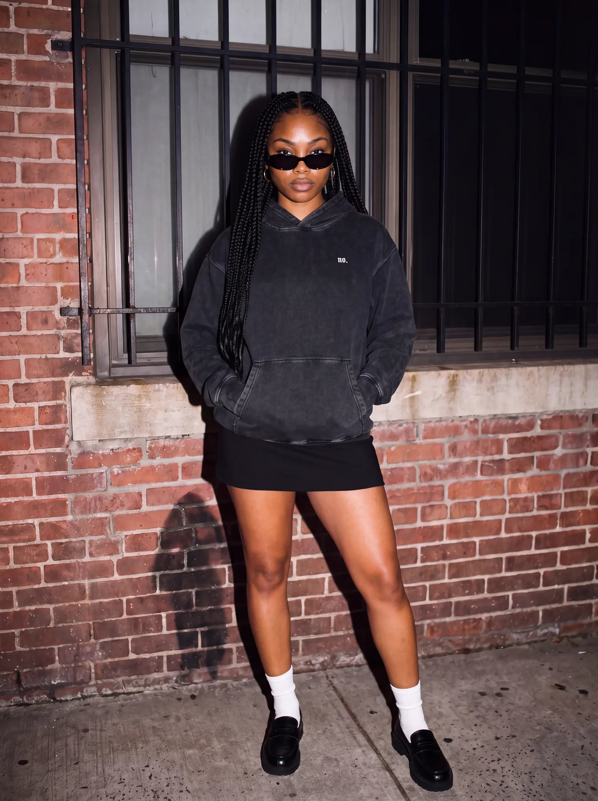 Woman standing in the black 'no.' oversized snow wash hoodie with a mini skirt