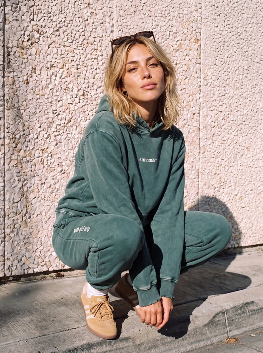 Woman crouching in the green "surrender." snow wash hoodie and matching joggers set