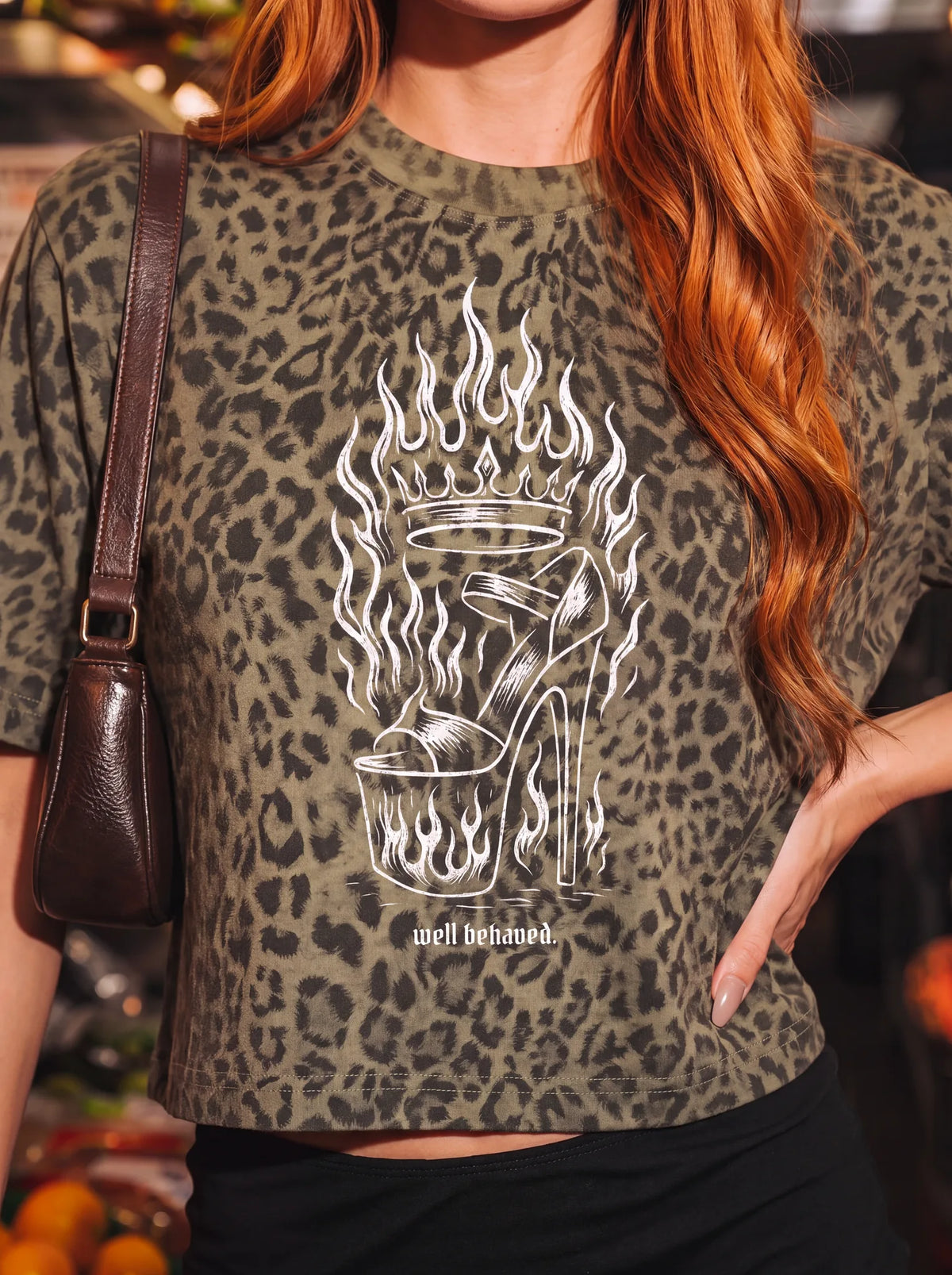 Model in a grocery store wearing the green leopard "well behaved." boxy tee with flaming high heel print