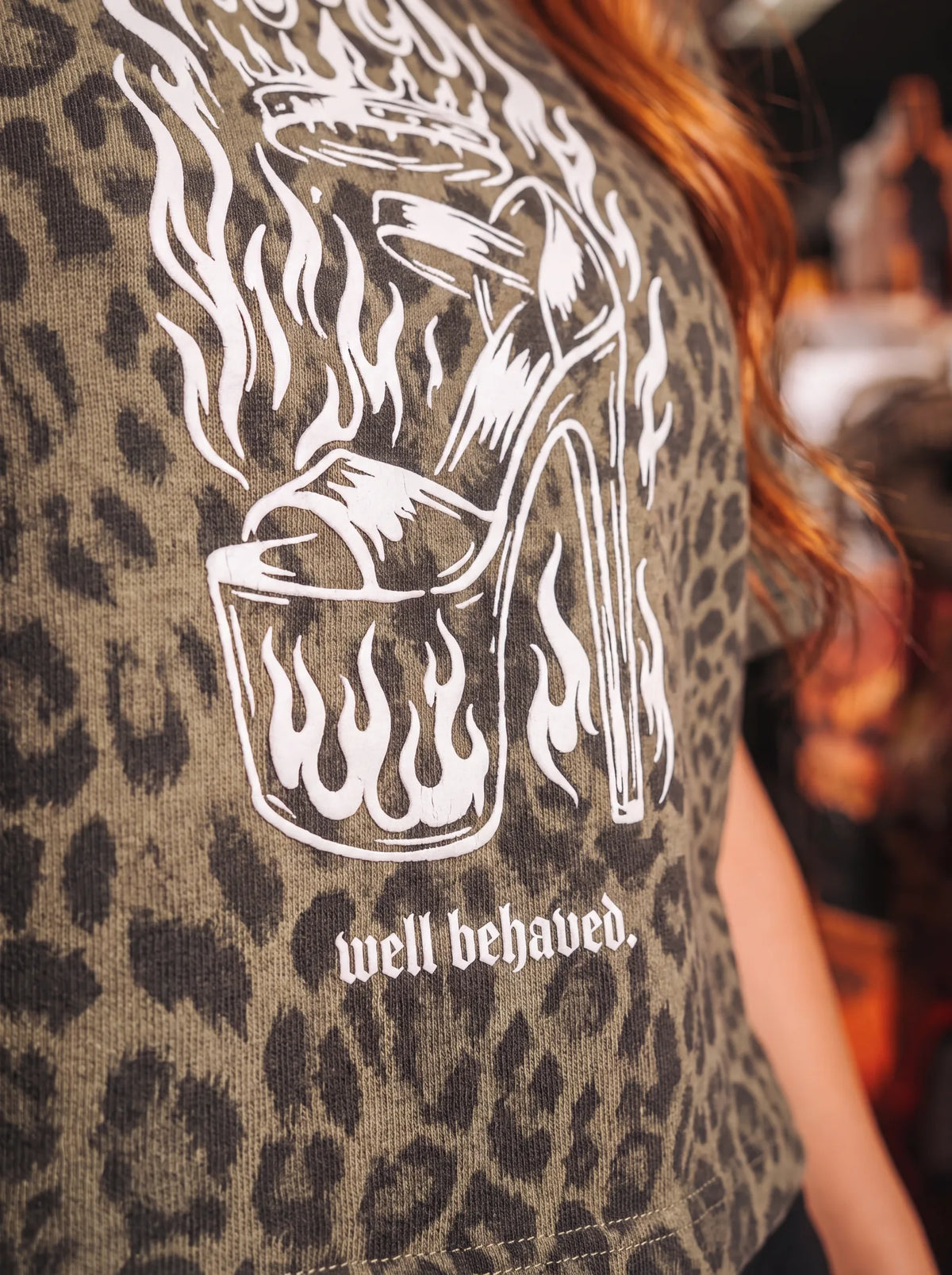 Close-up of the white flaming high heel screen print and "well behaved." caption on leopard cotton